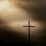 a cross on top of a hill under a cloudy sky